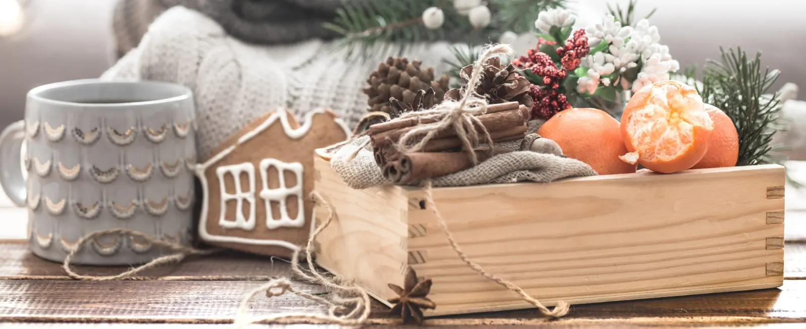 Detalle navideño con mandarinas, canela, piñas y una galleta de jengibre en una caja de madera, ambientación festiva para un alquiler vacacional