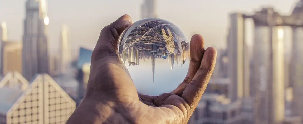 Mano sosteniendo una bola de cristal que refleja invertidos los rascacielos de una ciudad